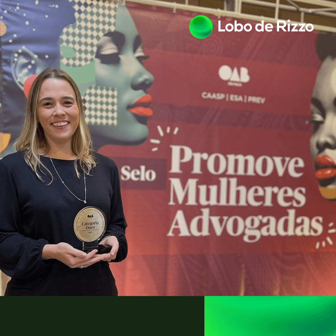 A foto mostra Thaís Alfonso, gerente de Diversidade e Inclusão do Lobo de Rizzo, uma mulher de pele clara, cabelos claros na altura do ombro, que veste uma blusa preta e que está em frente a um painel com os dizeres “Selo Promove Mulheres Advogadas”. O logo do Lobo de Rizzo está ao lado direito da imagem.